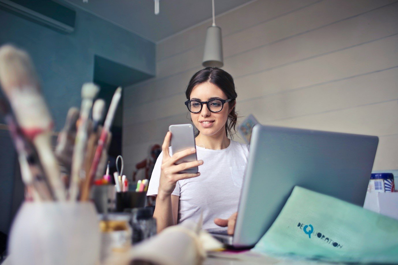 A person holding a phone and looking at a computer

Description automatically generated